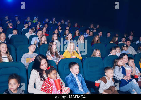 Frontview dei giovani usciti per guardare la gente interessante film in sala cinema. I ragazzi e le ragazze hanno un aspetto molto emotivo e felice. Modelli di indossare abiti colorati,mangiare popcorn, bere bevande gassate. Foto Stock