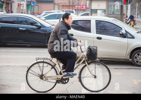 Xian, Cina - 8 Marzo 2018 - un uomo cinese cavalca la sua bicicletta su una strada trafficata di Xian, mento nella mattinata del 8 marzo 2018 Foto Stock