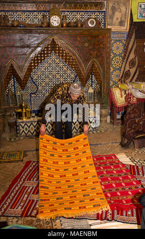 Il Marocco, Fes, Fes el Bali, Medina, negozio di antiquariato, venditore visualizzazione tappeti colorati Foto Stock