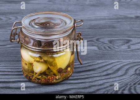 Vintage vasetto in vetro con spicchi di aglio in olio. Allium sativum. Retrò flip-top bottiglia con sott'aceto aromatico piccante verdure su uno sfondo di legno. Foto Stock