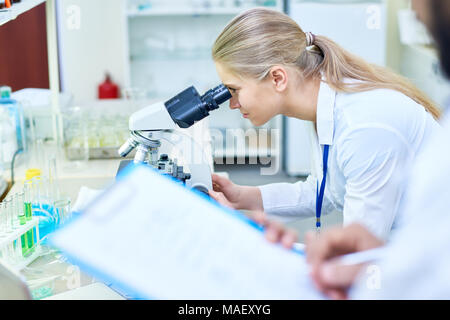 Serio studente di medicina analizzando il campione attraverso il microscopio Foto Stock