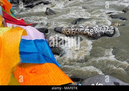 Rocce dipinte con parole di preghiera e la preghiera di bandiere nel fiume, Tagong, western Sichuan, Cina Foto Stock