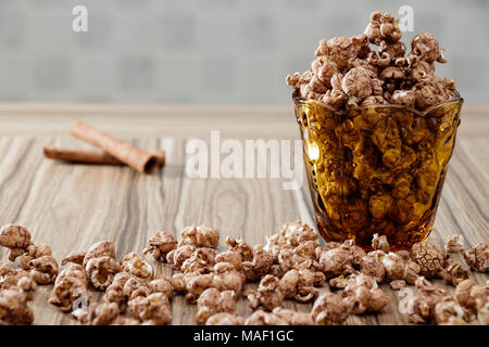 Il cioccolato aromatizzato popcorn in vetro di colore giallo e il marrone del legno tabella con sfondo di cannella Foto Stock
