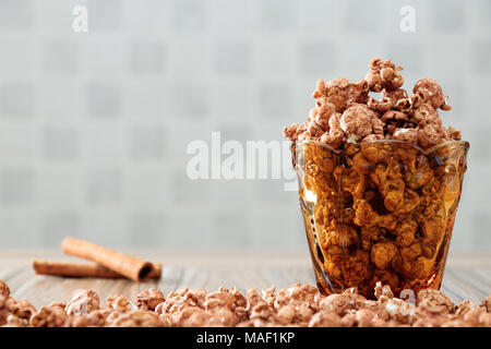 Il cioccolato aromatizzato popcorn in vetro di colore giallo e il marrone del legno tabella con sfondo di cannella Foto Stock