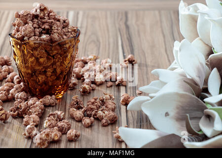 Aroma di cioccolato popcorn in vetro di colore giallo e marrone tavolo in legno con fiore bianco sullo sfondo Foto Stock