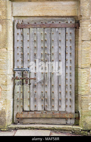 Di età compresa tra i forti porta di legno con i prigionieri di ferro arrugginito e cerniere, imbullonato chiuso. Incorniciato da muro in pietra. Foto Stock