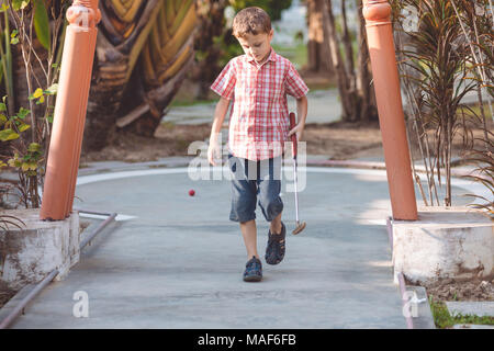 Happy little boy giocare mini golf giocare mini golf in un parco al giorno. Kid avendo divertimento all'aperto. Concetto di buon tempo libero. Foto Stock