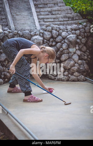 Felice bambina giocare mini golf giocare mini golf in un parco al giorno. Kid avendo divertimento all'aperto. Concetto di buon tempo libero. Foto Stock