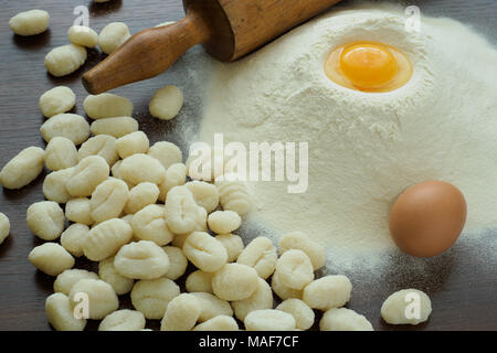 Materie gnocchi di patate con uova, farina e perno di rotolamento su di un tavolo di legno Foto Stock