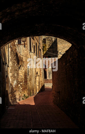 Guardando attraverso un portale scuro su un soleggiato lato medievale street Foto Stock