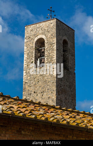 Close-up di un San Gimignano torre campanaria e piastrellate in primo piano sul tetto, circondata da un cielo blu brillante, Toscana, Italia Foto Stock