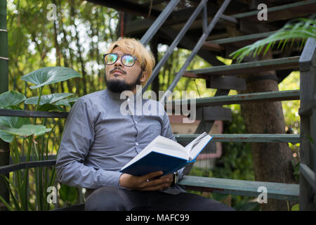 Giovani hipster barba uomo la lettura di libri nel giardino di casa con la natura. Il concetto di istruzione. Foto Stock