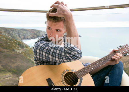 Bello il musicista a suonare la chitarra su Hotel balcone con vista oceano in background. Foto Stock