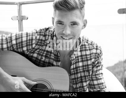 Bello il musicista a suonare la chitarra su Hotel balcone con vista oceano in background. Foto Stock