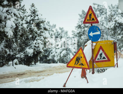 In costruzione i segni nella neve. Simboli di avvertenza sulla strada della ricostruzione. Strada innevata e sfondo di foresta. Foto Stock