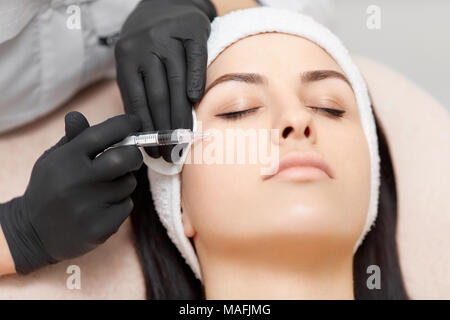 Close-up di bella donna con gli occhi chiusi di ottenere l'iniezione nel suo volto, rendendo la sua pelle sollevata e liscia. Mani di professionisti cosmetologo hol Foto Stock