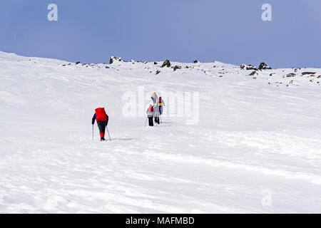 Gruppo di escursionisti sulla coperta di neve montagna pendenza sotto un luminoso cielo blu Foto Stock