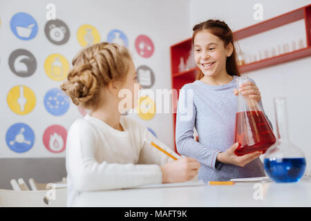 Upbeat ragazza in chat con il suo amico durante la chimica classe Foto Stock