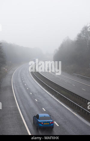 Autocarri e veicoli che percorrono un'autostrada britannica bagnata e nebbiosa, circondata da boschi. Condizioni meteorologiche tipiche del Regno Unito Foto Stock