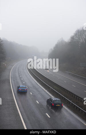 Autocarri e veicoli che percorrono un'autostrada britannica bagnata e nebbiosa, circondata da boschi. Condizioni meteorologiche tipiche del Regno Unito Foto Stock