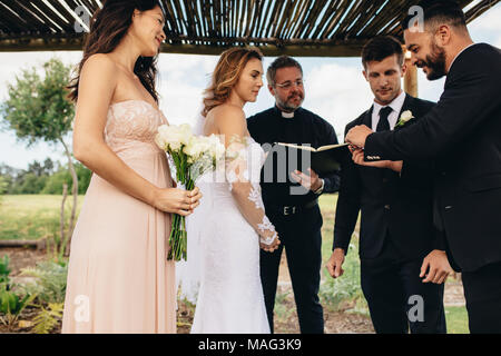 Cerimonia di nozze tradizionale del giovane all'esterno. Miglior uomo dando gli anelli di nozze per lo sposo prima di anelli cerimonia di exchange. Foto Stock