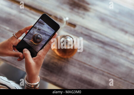 In prossimità di una donna di catturare foto di una teiera in vetro utilizzando un telefono cellulare per il suo cibo blog. Blogger alimentare a scattare foto per il suo blog. Foto Stock