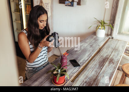 Donna di scattare le foto di un smoothie posto accanto a un vaso di fiori utilizzando una telecamera professionale per il suo cibo blog. Blogger alimentare a scattare foto per il suo blog Foto Stock