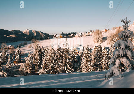 Sunny inverno mattina nei monti Tatra. Montagna Collina villaggio con casette di legno e gli alberi coperti di uno strato spesso di neve fresca. Zakopane - Polonia Foto Stock