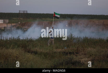 Un manifestante palestinese sventola la bandiera nazionale tenendo il coperchio dalla Israeli gas lacrimogeni sparati durante gli scontri lungo il confine tra Israele e la striscia di Gaza, nella parte orientale di Gaza City, nella Striscia di Gaza, 02 aprile 2018. Foto: Wissam Nassar/dpa Foto Stock