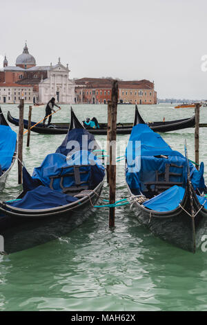 Vista verticale delle gondole attraccate e gondoliere in background in Venezia Foto Stock