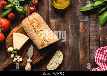 Il cibo italiano su legno rustico sfondo, vista dall'alto. Il formaggio parmigiano reggiano, ciabatta, bruschette, basilico, olio d'oliva e pomodori. Cucina italiana Foto Stock