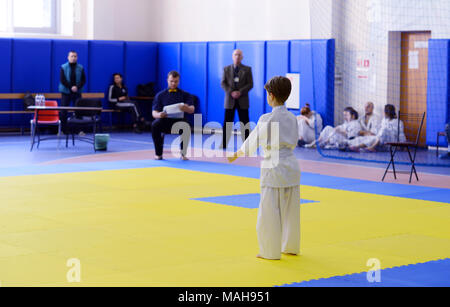 La concorrenza tra i bambini nel karate,kata.7-8 anno vecchio ragazzo sta con la sua schiena sul tatami, in fudo dati egli è pronto per eseguire in kata Foto Stock