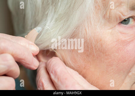 Close Up di Senior donna mettendo in aiuto dell'udito Foto Stock