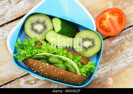Pranzo sano scatola contenente formaggio di segale rotolo, bastoncini di cetriolo e kiwi Foto Stock
