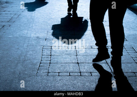 Silhouette ombre di tre persone che camminano da soli su una strada di città di notte Foto Stock