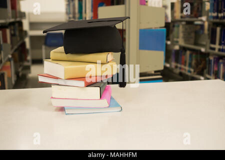 Un mortarboard e graduazione di scorrimento, legate con un nastro rosso, stack sul libro. Il concetto di istruzione. Foto Stock