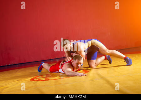 Due giovani lottatori di uomo in rosso e blu di wrestling uniforme su un giallo tappeto di wrestling in palestra. Alle prese. Foto Stock