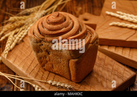 Bellissimo il pane fatto in casa su una superficie strutturata di legno. Una bella combinazione del colore di sfondo di legno e pane. Close-up. Foto Stock