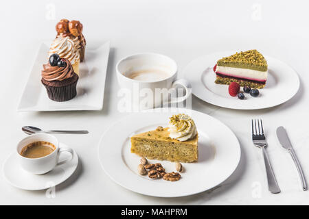 Vista superiore della disposizione dei pezzi di varie torte su piatti e tazze di caffè e tortine isolato su bianco Foto Stock