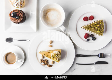 Vista ravvicinata della disposizione dei pezzi di varie torte su piatti e tazze di caffè e tortine isolato su bianco Foto Stock