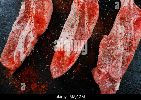 Carne di maiale cruda sulla pietra scura sullo sfondo, bistecche di carne fresca dalla vista superiore Foto Stock