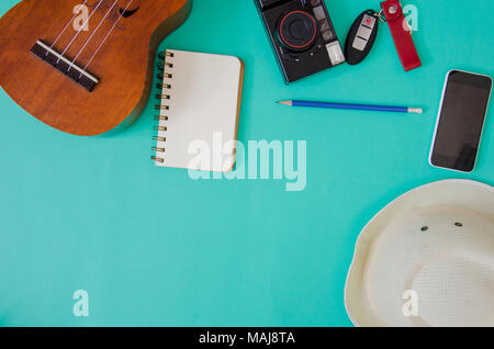 Accessori per viaggiatori. Hat, ukulele, matite e quaderni. e telefono sullo sfondo verde. Foto Stock