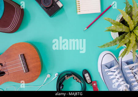 Accessori per viaggiatori. Scarpe, , ukulele, matite e quaderni e telefono su sfondo verde. Foto Stock