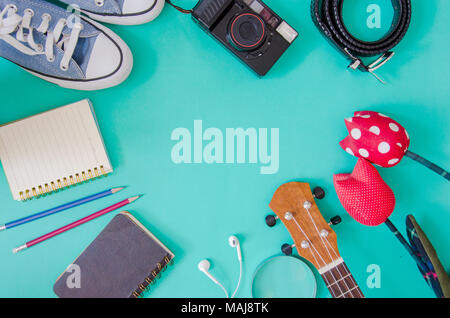 Accessori per viaggiatori. Scarpe, , ukulele, matite e quaderni e telefono su sfondo verde. Foto Stock