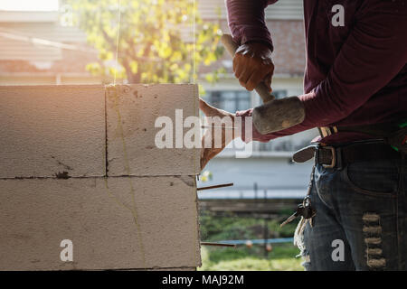 Mason lavoratore la costruzione di muri esterni, egli usando un martello di gomma per la posa in opera di mattoni in cemento Foto Stock