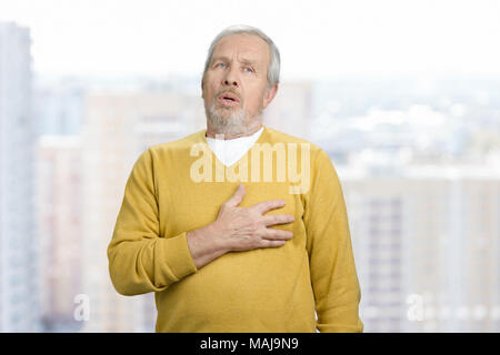 Ritratto di nonno vecchio toccando il suo petto. Sensazione di dolore nel cuore. Città urbana dello sfondo. Foto Stock