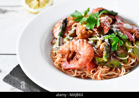 Spaghetti frutti di mare o un piatto di pasta con gamberi e asparagi verdi e prezzemolo e guarnire. Piastra bianca su una tavola di legno, mangiare sano scena. Foto Stock