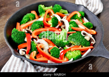 Mangiare sano scena con le verdure in una padella di ferro o pentola di cottura. Broccoli, peperone rosso, carote e funghi bianco. Foto Stock