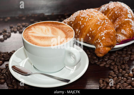 Cappuccino con brioche e caffè in grani Foto Stock