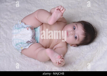 Piccolo bambino gioca con i suoi piedi su bianco soffice coltre. Prodotti tessili e biancheria da letto per bambini. Foto Stock